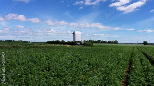 Drone shot circling around a windmill without sails surrounded by fields.