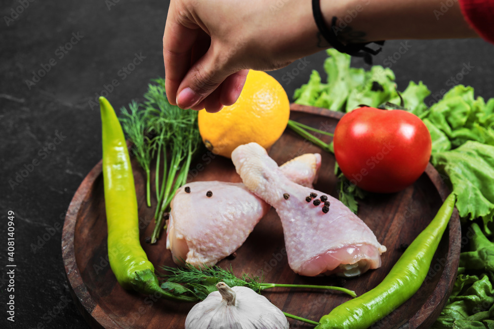 Woman hand holding a wooden plate of raw chicken legs with fresh vegetables Woman hand holding a wooden plate of raw chicken legs with fresh vegetables