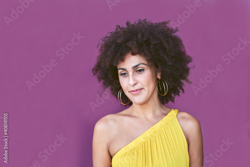 Woman with afro hair. She has a yellow dress and behind is a purple background