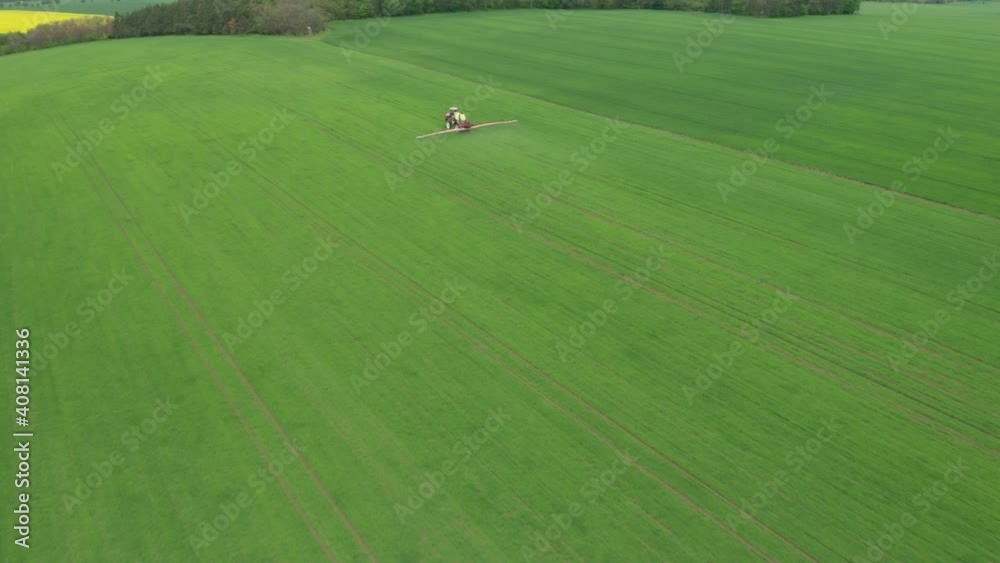 Aerial view of farming tractor plowing and spraying green wheat field. Protection of crop with applying of pesticides, herbicides or insecticides Aerial view of farming tractor plowing and spraying green wheat field. Protection of crop with applying of pesticides, herbicides or insecticides