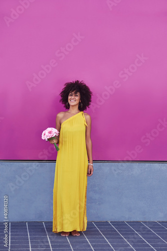 
Woman with afro hair. She has a yellow dress and behind is a purple background