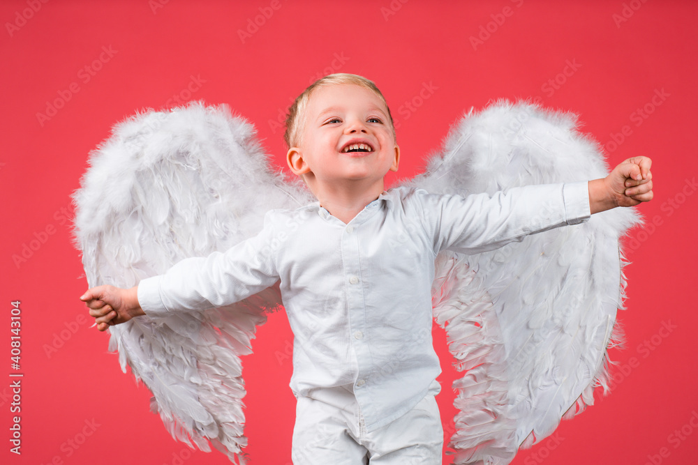 Obraz premium Excited angel little boy with white wings. Happy angelic children boy laughing. Cute kid with white wings. Adorable child cupid isolated on red. Valentines day card, baner copy spase. Funny face.