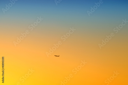 a plane in the distance flies in the sky at sunset