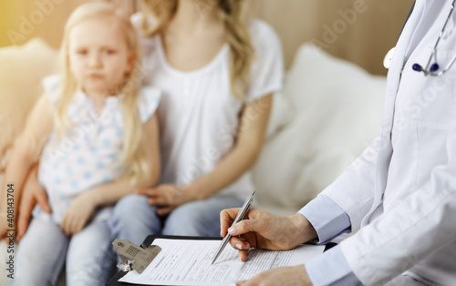 Doctor and patient. Pediatrician using clipboard while examining little girl with her mother at home. Sick and unhappy child at medical exam © rogerphoto