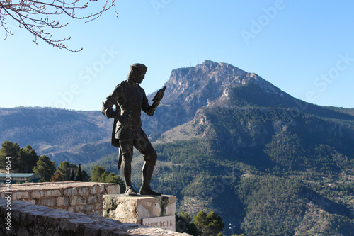 Paisaje montañoso con una escultura en primer plano. Se trata de un escritor español que aparece leyendo un libro.