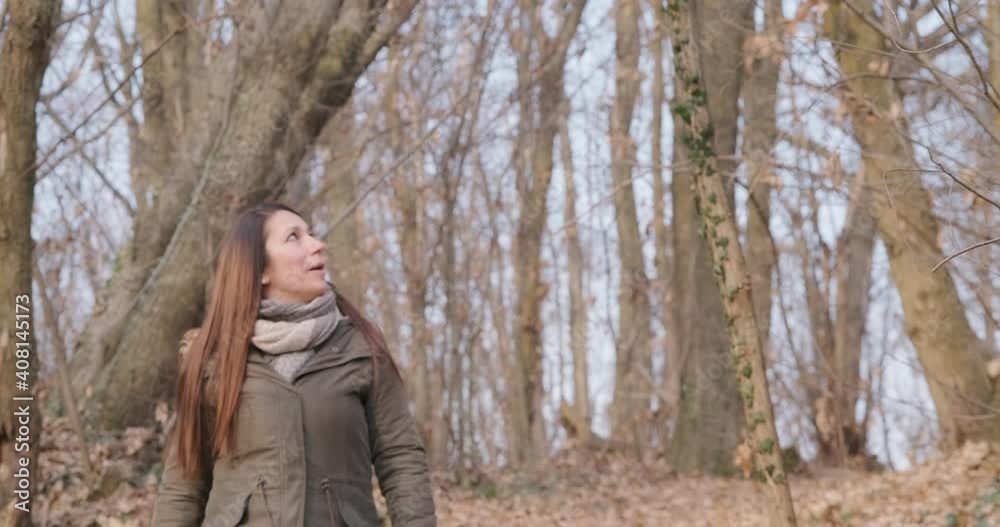 Brunette Woman Wearing Winter Jacket Walking In Forest And Looking Around On A Sunny Day. - slow motion Brunette Woman Wearing Winter Jacket Walking In Forest And Looking Around On A Sunny Day. - slow motion