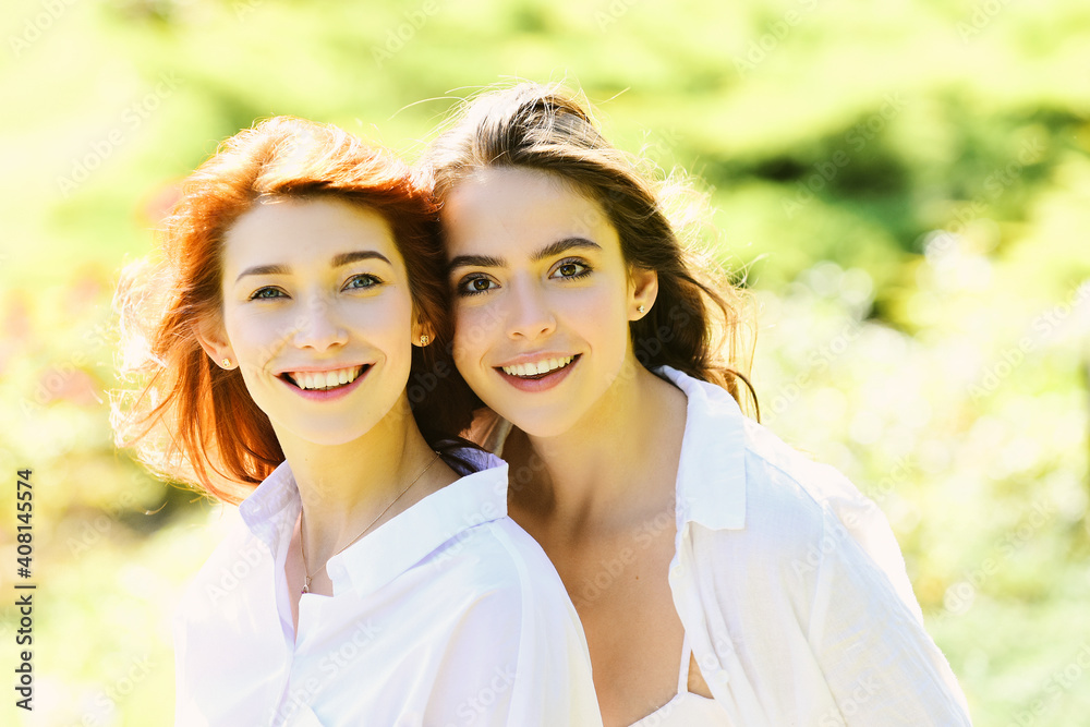 Portrait of two cheerful young women standing together and looking at camera over green spring background. Portrait of two cheerful young women standing together and looking at camera over green spring background.