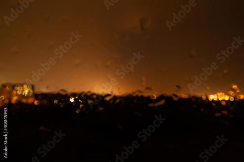 Rain and lightning glow behind glass out of focus. Night city lights