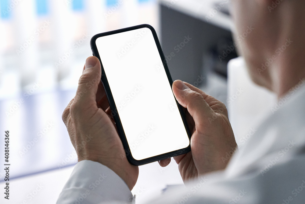 Foto Stock Male doctor holding cell phone in hands using blank white mockup  screen technology ehealth mobile app for medical healthcare telemedicine  ads, e telehealth online applications. Over shoulder view | Adobe