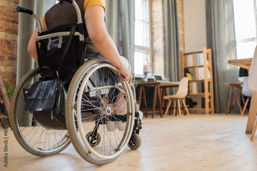 Obraz premium Back view of young disable female sitting in wheelchair in the center of office