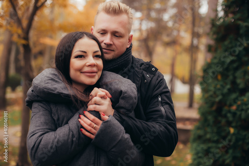 A man hugs and holds the hand of his girlfriend as she smiles