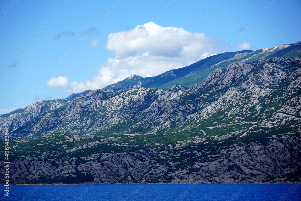 Mountain with green hills near blue ocean and white clouds on the sky