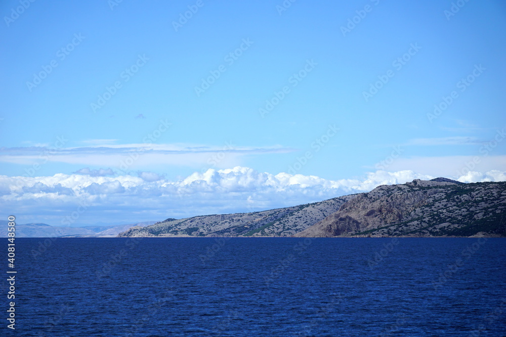 Rocky island surrounded with blue ocean water and sky with white clouds
