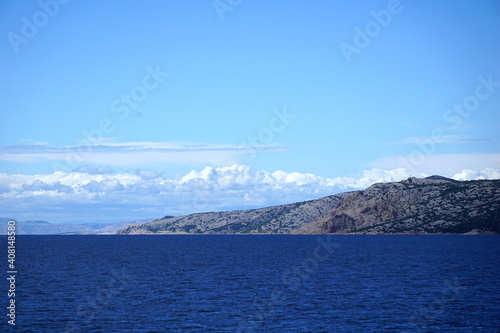 Rocky island surrounded with blue ocean water and sky with white clouds © Happy window
