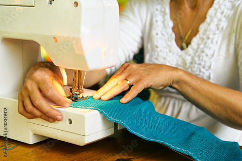 Mujer cosiendo con maquina de cocer eléctrica. Manos de mujer haciendo manualidades de costura 