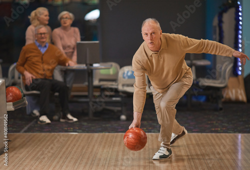 Fotografie Full length portrait of active senior man playing bowling and throwing ball by l