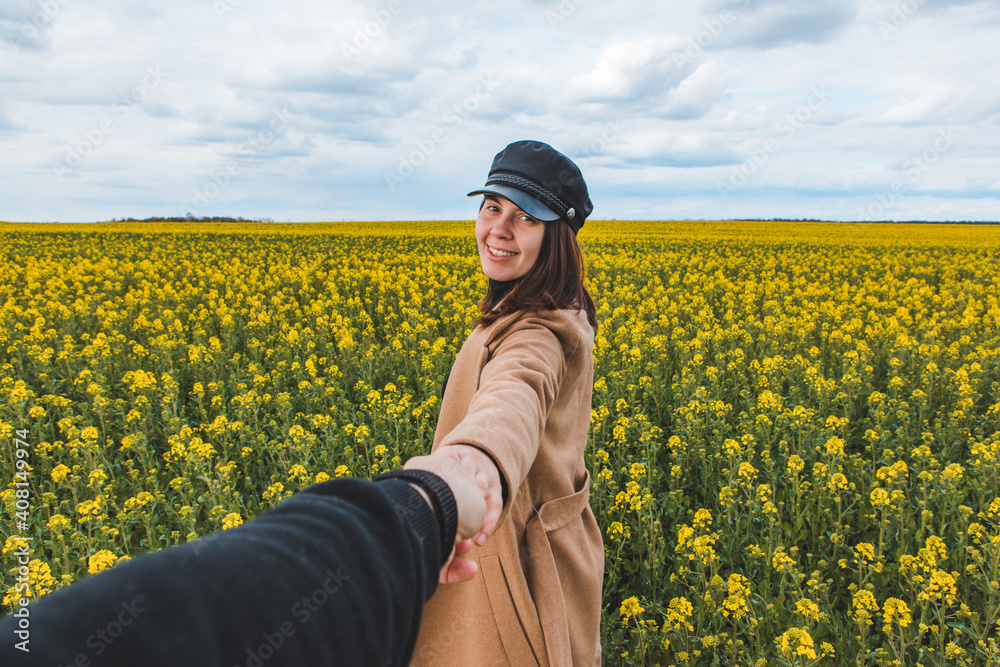 follow me concept woman holding man hand leading to yellow rapeseed field