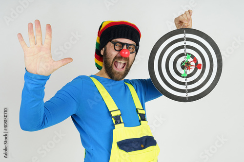 The clown holds a target in his hands, shows the result of dart shooting, with the second hand shows a gesture - class. photo