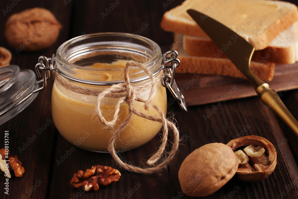 Vegetarian traditional breakfast. Natural nut butter in a glass jar, a golden knife, walnuts and sandwiches with toast on a wooden brown background. Vegetarian traditional breakfast. Close up Vegetarian traditional breakfast. Natural nut butter in a glass jar, a golden knife, walnuts and sandwiches with toast on a wooden brown background. Vegetarian traditional breakfast. Close up