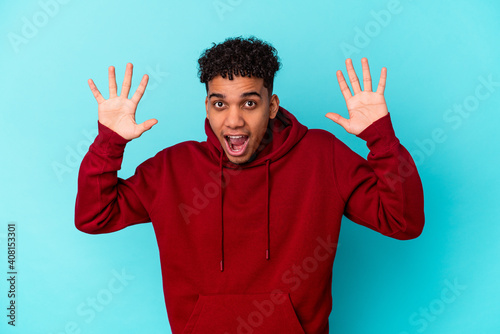 Young african american curly man isolated on blue receiving a pleasant surprise, excited and raising hands.