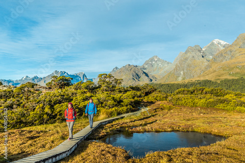 New Zealand Hiking. Young hiking couple walking on trail at Routeburn Track during sunny day. Hikers are carrying backpacks while tramping Key Summit Track in Fiordland National Park in New Zealand. photo