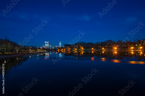 Lake in park during blue hour with illuminated office buildings and apartment blocks