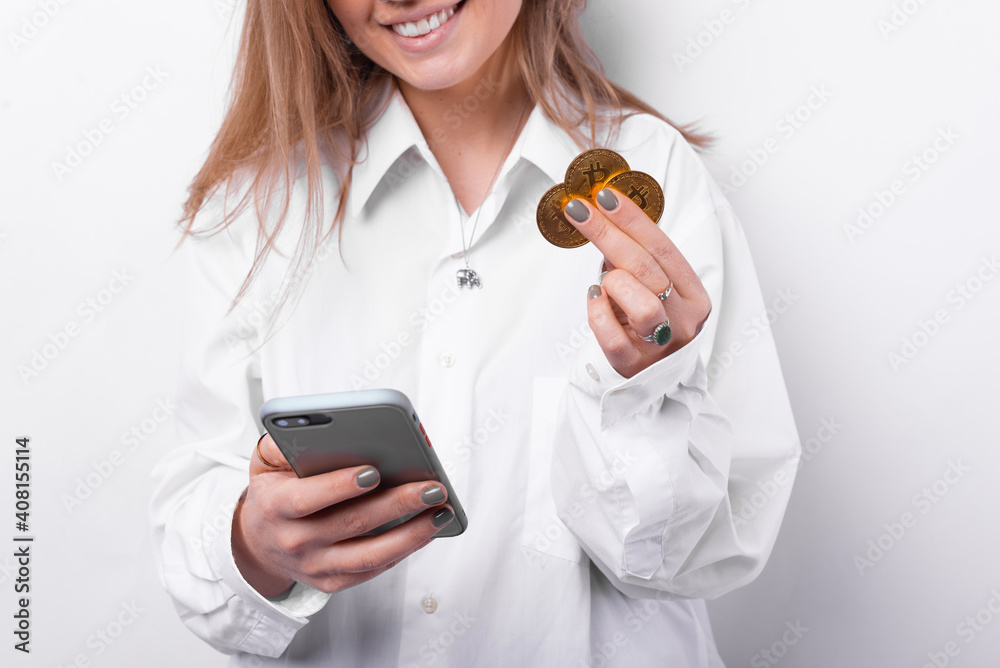 Close up photo of cheerful woman holding smartphone and bitcoins. Close up photo of cheerful woman holding smartphone and bitcoins.