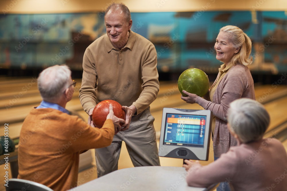 Fototapeta premium Group of senior people playing bowling together while enjoying active entertainment at bowling alley, copy space