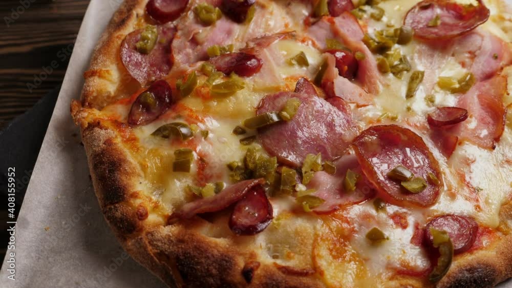 One salami and bacon pizza on black slate platter rotating, closeup One salami and bacon pizza on black slate platter rotating, closeup