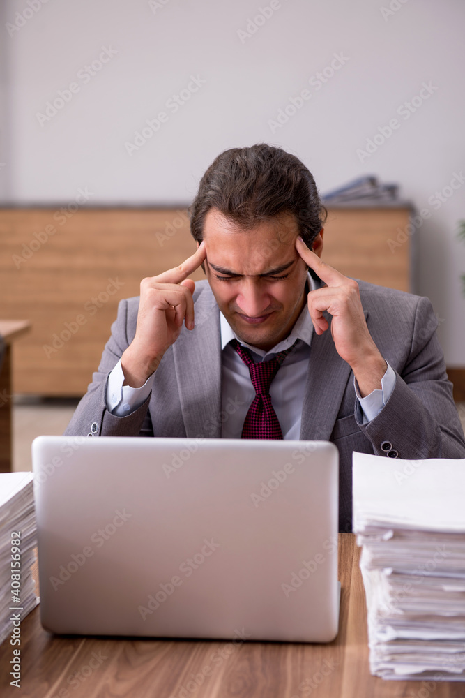Young male employee unhappy with excessive work in the office Young male employee unhappy with excessive work in the office