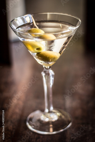 Martini cocktail alcohol drink beverage with olives and bokeh background on a wooden table