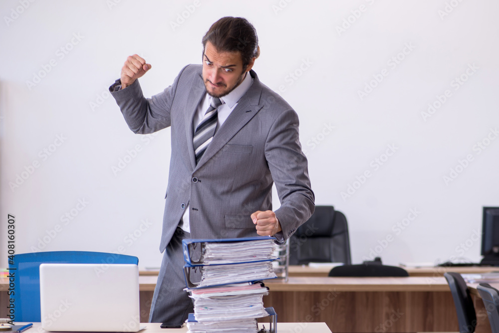 Young male employee unhappy with excessive work in the office Young male employee unhappy with excessive work in the office