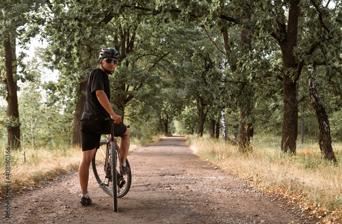 Professional cyclist in a helmet on bicycle stands on the countryside road.