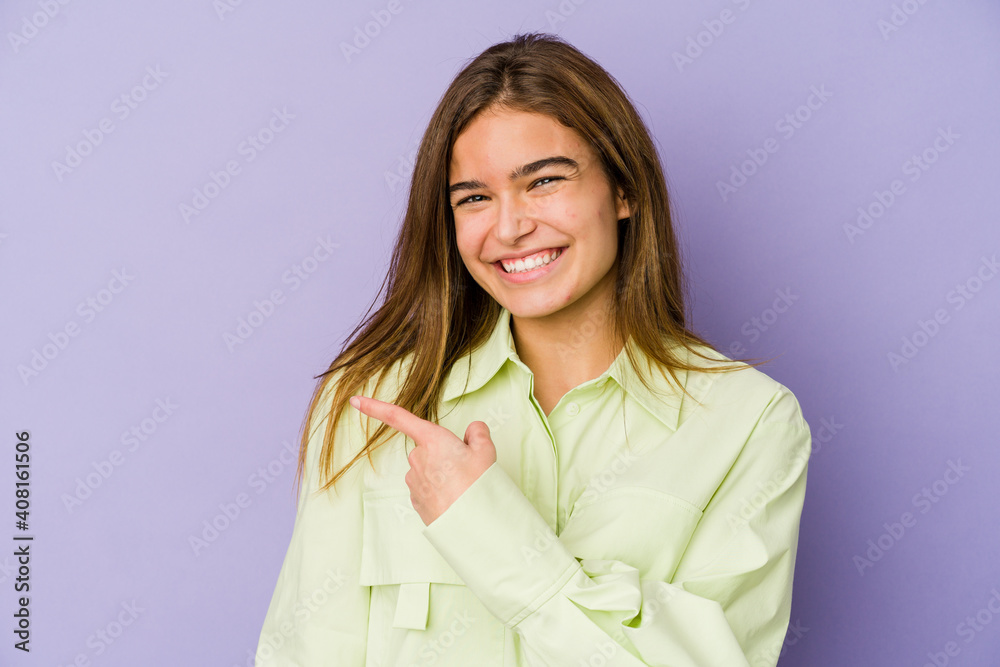 Young skinny caucasian girl teenager on purple background smiling and pointing aside, showing something at blank space. Young skinny caucasian girl teenager on purple background smiling and pointing aside, showing something at blank space.