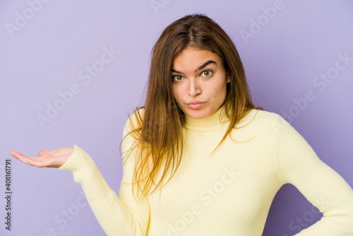 Young skinny caucasian girl teenager on purple background showing a copy space on a palm and holding another hand on waist.