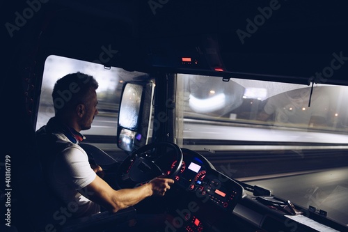 A handsome driver at the wheel of a truck is driving his goods at night. Truck driver job.