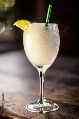 Frozen Passionfruit Vodka Slushy Daiquiri cocktail alcohol drink beverage with lemon, straw and bokeh background on a wooden table