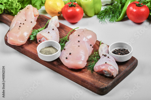 Wooden plate of raw chicken fillet and legs with spices and vegetables on white table. Close up