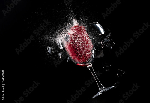 A glass of wine explodes and shatters into pieces with splashes and splashes on a black background