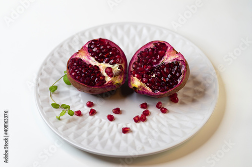 Two halves of fresh ripe pomegranate on a white plate, close-up..