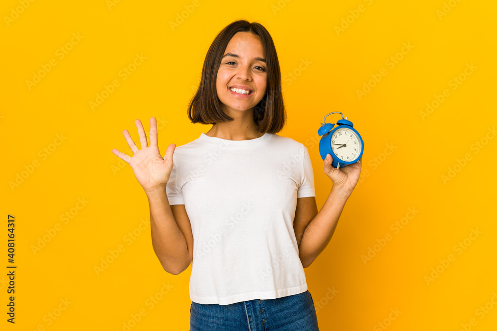 Young hispanic woman holding a megaphone smiling cheerful showing number five with fingers. Young hispanic woman holding a megaphone smiling cheerful showing number five with fingers.