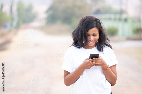 beautiful african woman using her phone outside on a bright sunny day, with blurred background