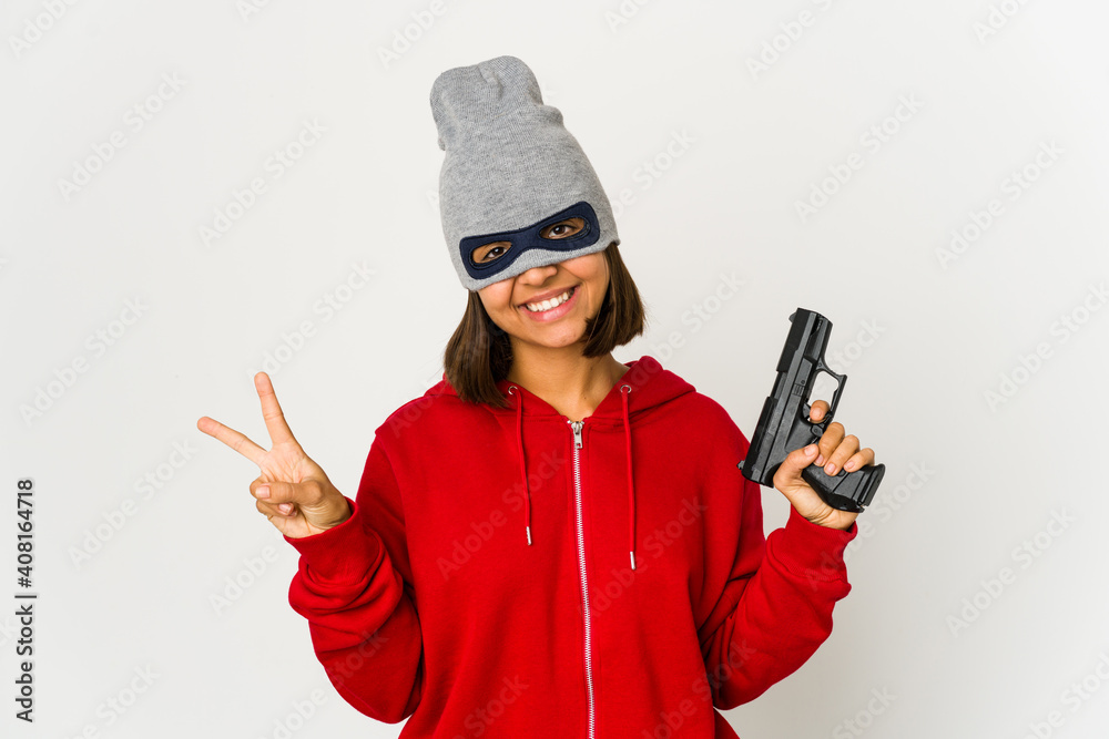 Young robber hispanic woman wearing a mask joyful and carefree showing a peace symbol with fingers.