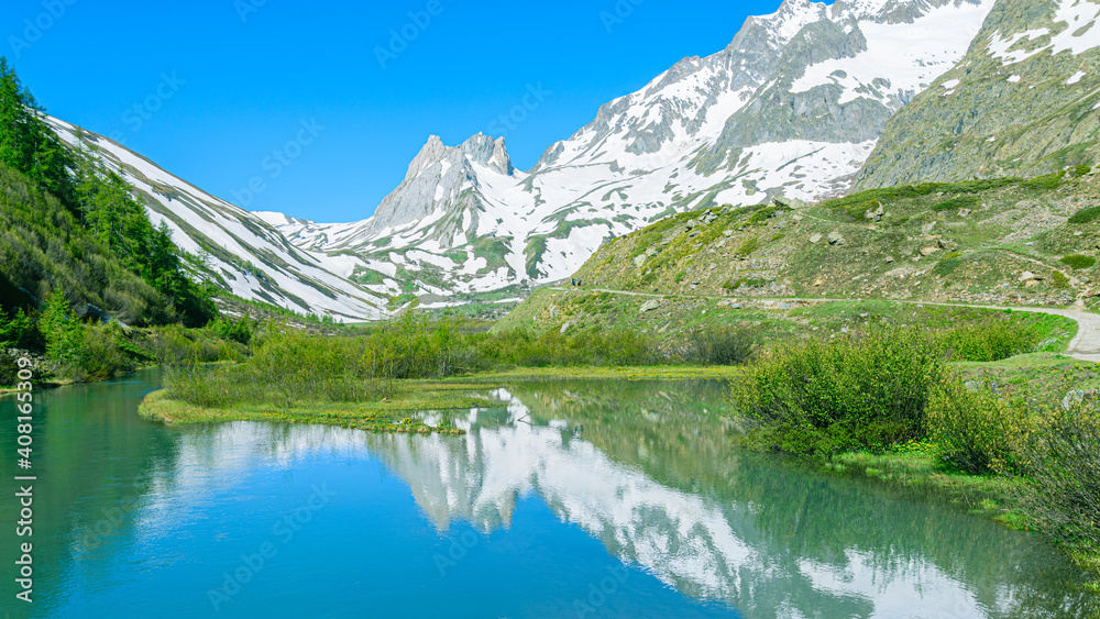 Mountains peaks mirroring in the lake showing symmetry. Mountains are full of snow and the water is calm. Val Veny, Italy