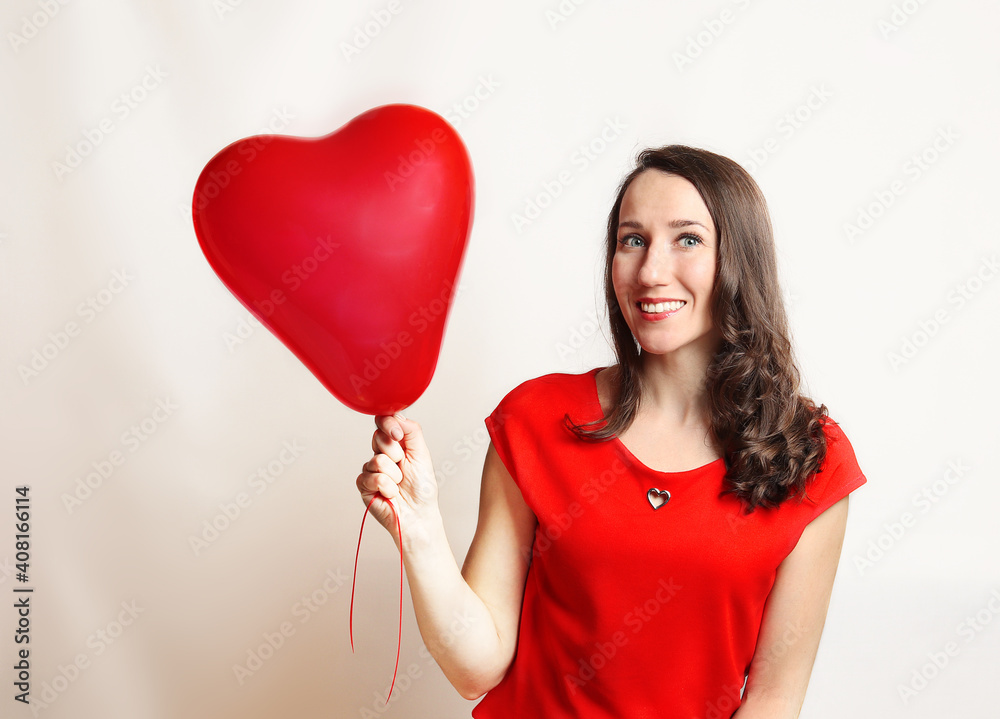 Smiling pleased caucasian girl posing with a red ball in the shape of a heart on white background. Beautiful happy young woman on a birthday holiday, Valentine's day, Mothers day. Close-up Smiling pleased caucasian girl posing with a red ball in the shape of a heart on white background. Beautiful happy young woman on a birthday holiday, Valentine's day, Mothers day. Close-up