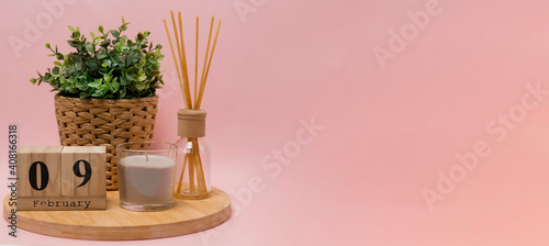 calendar. 9 february composition from a wooden calendar, a flower in a wicker pot, a gray candle in a glass candlestick and an aroma diffuser on a light pink background banner business