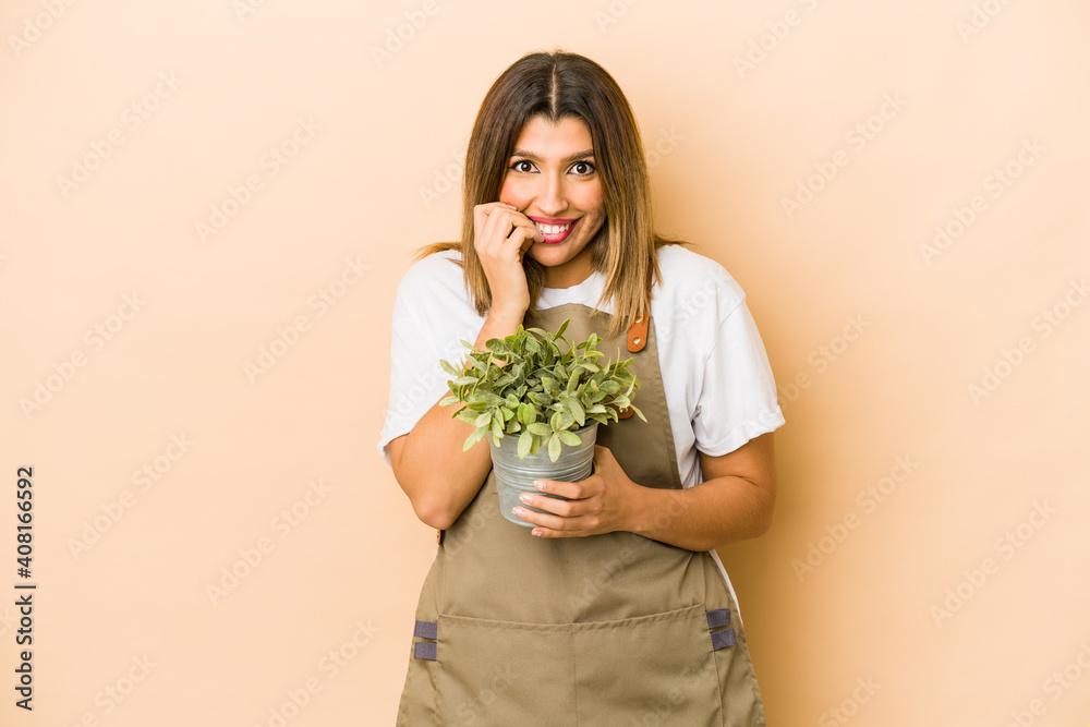 Young indian gardener woman holding a plant isolated biting fingernails, nervous and very anxious.