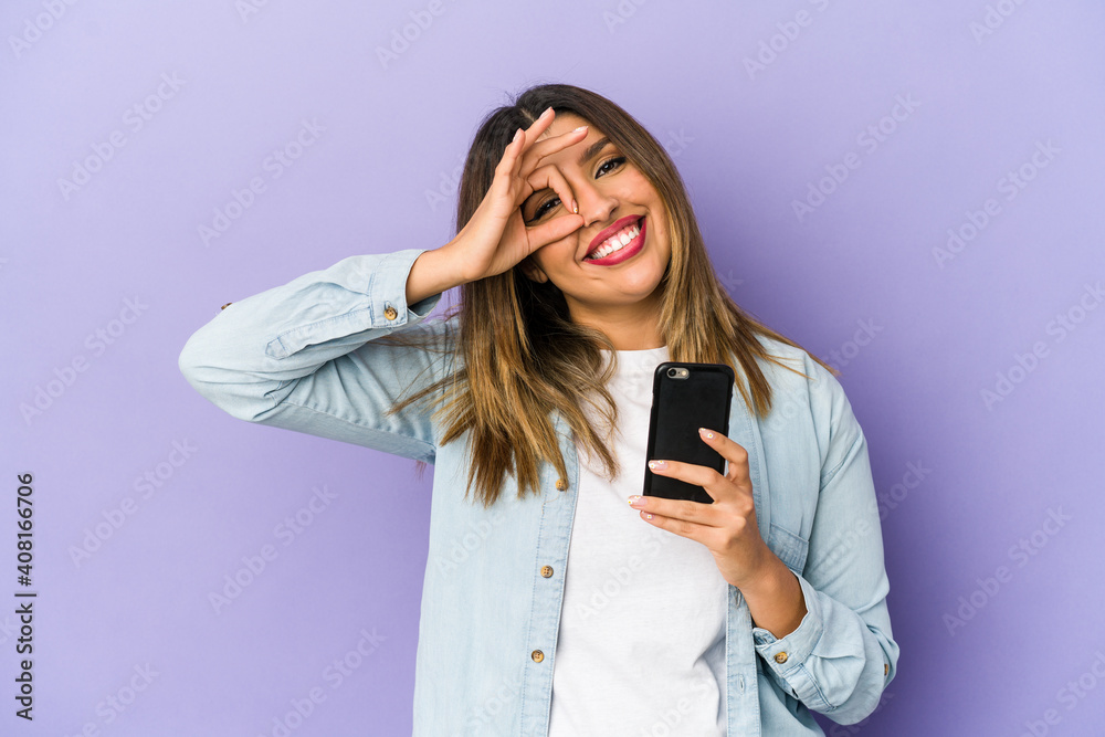 Young indian woman holding a phone isolated excited keeping ok gesture on eye. Young indian woman holding a phone isolated excited keeping ok gesture on eye.