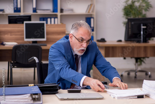 Old businessman employee in wheel-chair working in the office