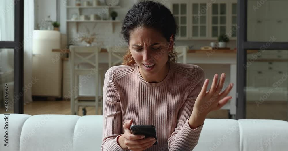 Confused young woman looking at mobile phone screen, feeling stressed of getting message with unpleasant scam news. Unhappy millennial caucasian lady dissatisfied with bad smartphone device work.